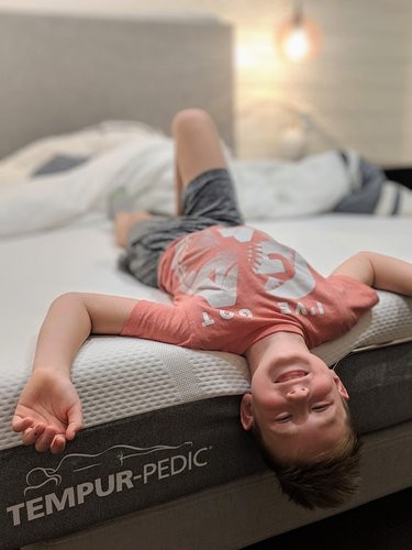 A laughing child playfully hanging off a Tempur-Cloud mattress
