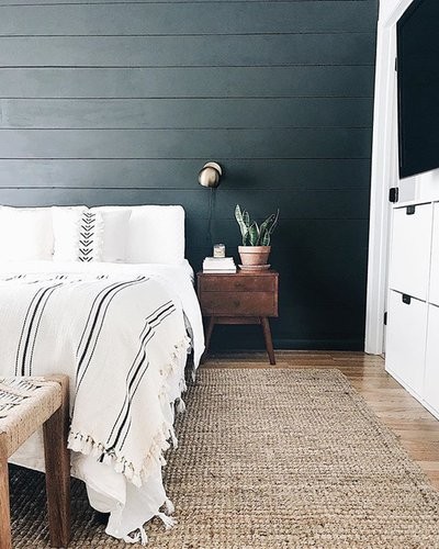 Half of a bed in a styled room, next to a bedside table with a plant upon it