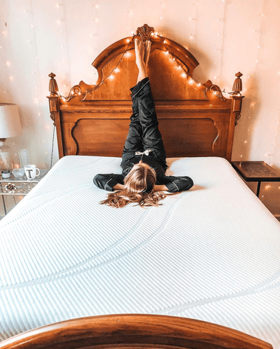 A woman in her silk pajamas lying on a mattress with her feet up on the headboard