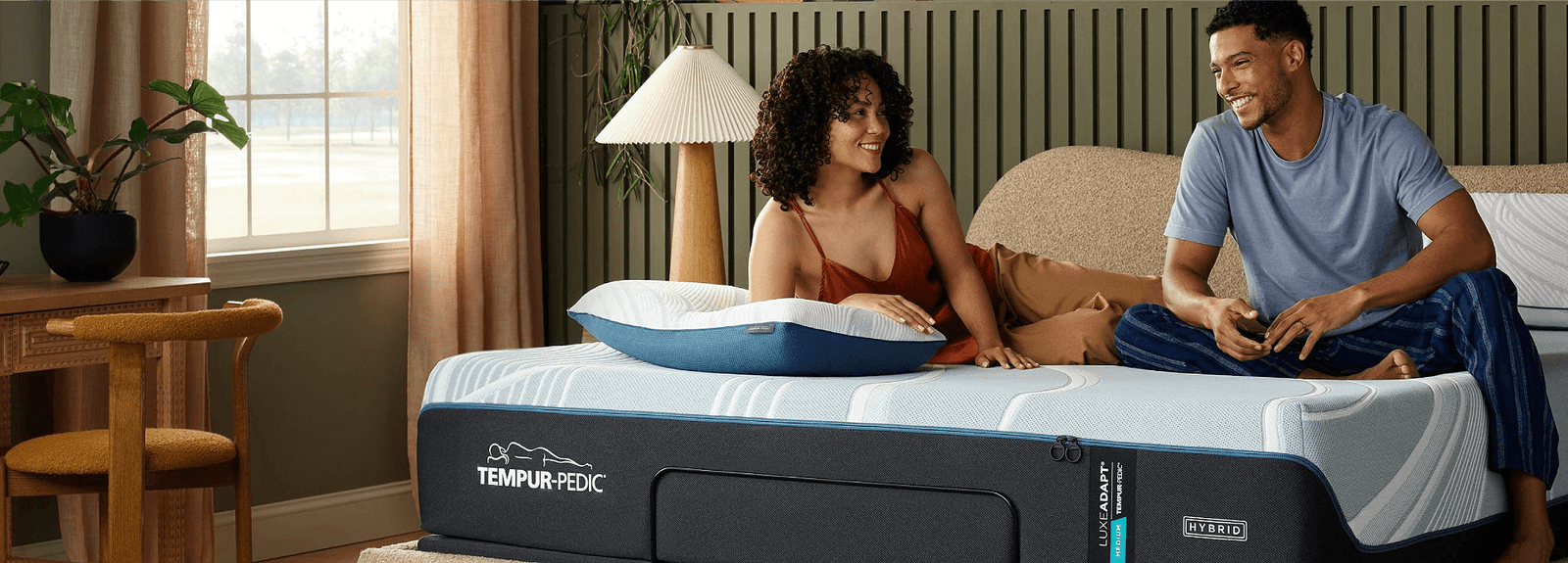 A couple sitting on a mattress with an Adapt pillow