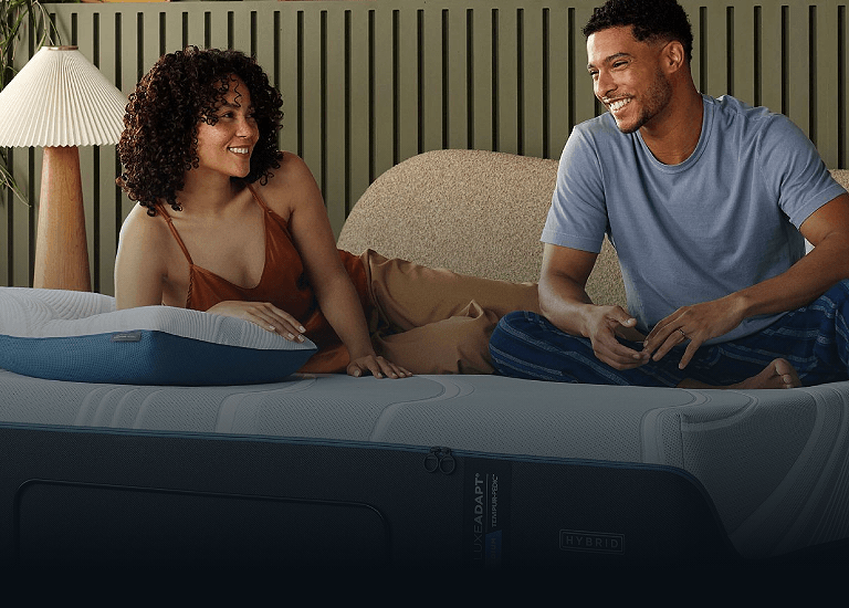 A couple sitting on a mattress with an Adapt pillow