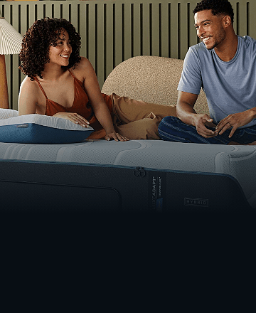 A couple sitting on an Adapt mattress with an Adapt pillow
