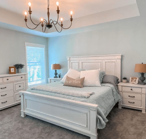 Bed with blue bedding sitting on white wooden bed frame in light blue room