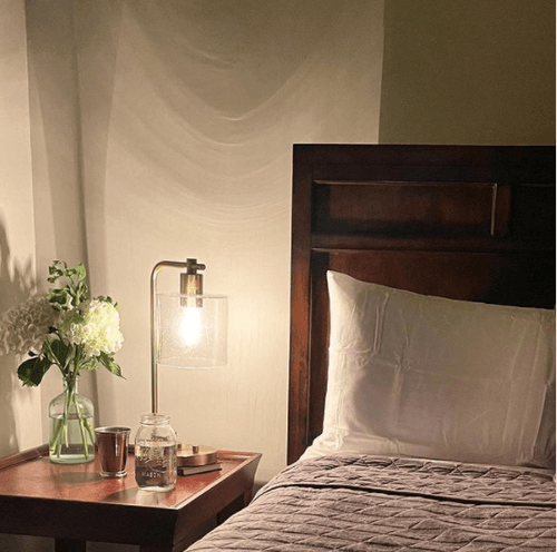 Decorated bed next to side table and lamp with warm lighting