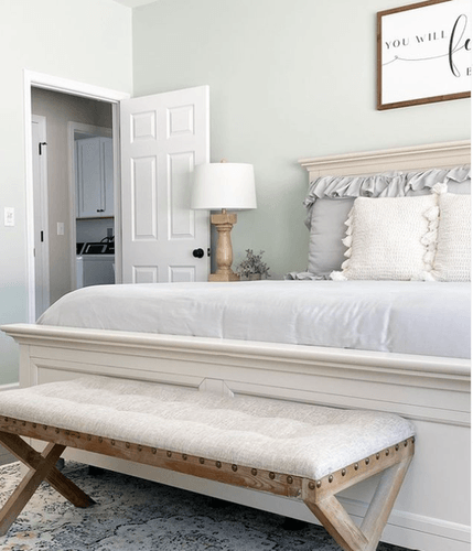 Decorated bedroom with pale green walls, light gray bedding, and a decorative bench