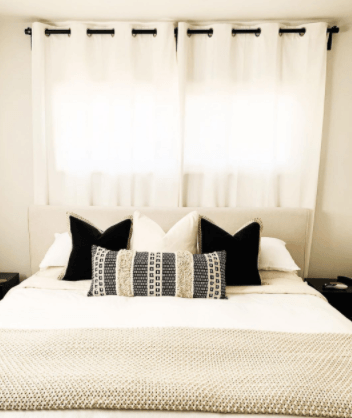 Mattress with white bedding, black and white pillows, and white curtains.png