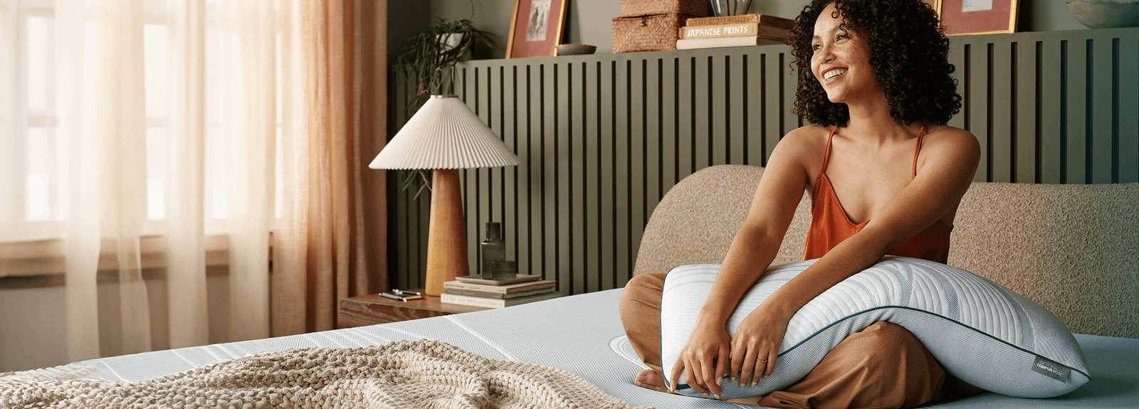 Woman sitting on a mattress holding an Adapt pillow