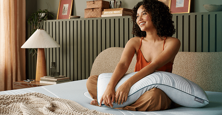 Woman sitting on a mattress holding an Adapt pillow