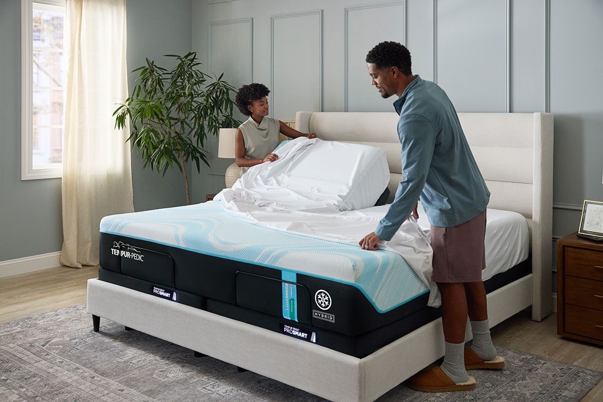 Couple putting sheets on TEMPUR-Breeze mattress in decorated room