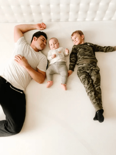 A father and two smiling children laying on a Tempur-Cloud mattress