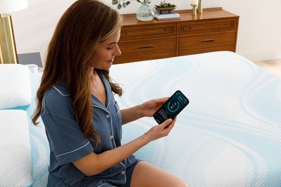Women sitting on TEMPUR-Breeze mattress looking at Sleeptracker-AI App on smartphone