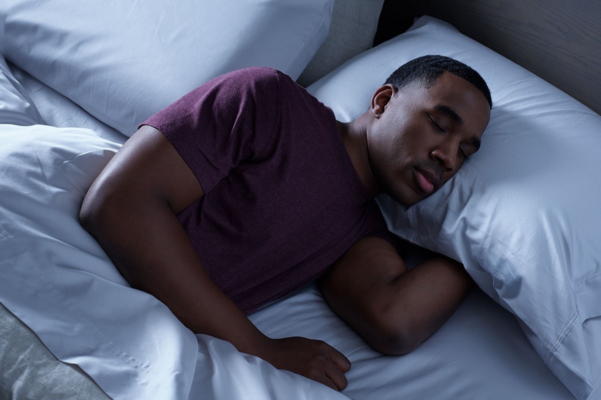 Man sleeping in dark room wearing a maroon shirt