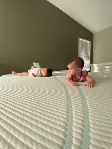 Two babies lying on Tempur-Pedic mattress in front of olive green wall