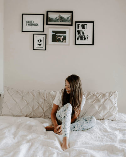 Woman sitting on her bed looking away from the camera with picture frames on the wall behind her