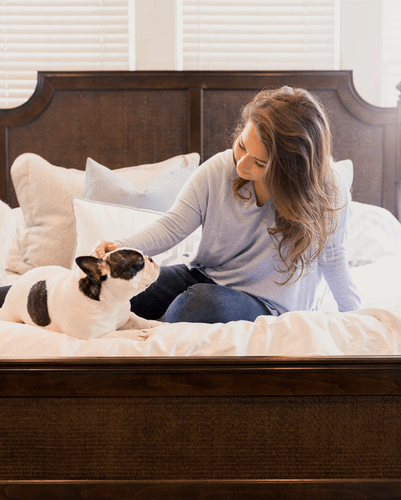 Bedroom setting with a woman sitting on her bed, petting her dog