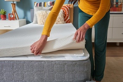 A person putting a Tempur-Pedic topper on a bed