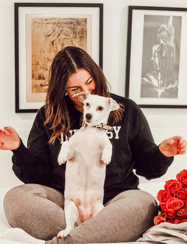 Woman sitting down smiling behind dog standing on bed