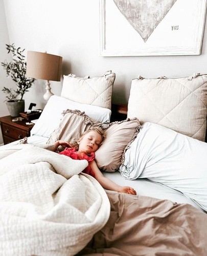 little girl asleep in bed with cream colored pillows and blankets