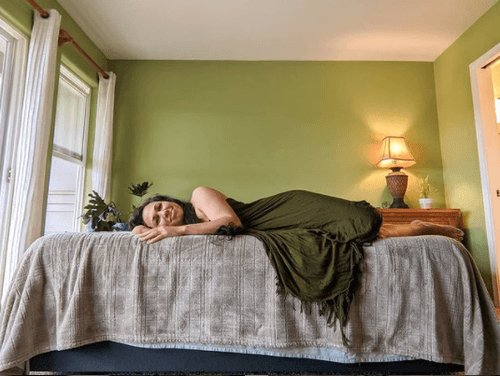 woman in green dress lying on side on mattress in bedroom with green walls.png